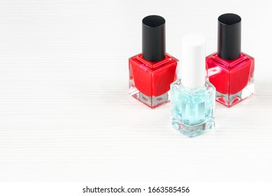 Close-up image of Two Red nail polish bottles and one colorless nail polish bottle on white wooden background.