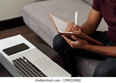 Close-up Image Of University Student Watching Online Webinar On Laptop And Taking Notes In Copybook