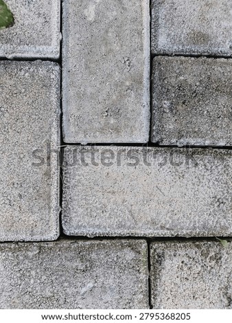 A close-up image of weathered gray paving stones arranged in a neat pattern. The rough texture and slight color variations create a simple yet detailed view of the outdoor surface.