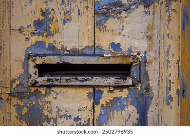 Closeup image of a weathered, peeling paint on an old wooden door with a vintage mail slot, perfect for backgrounds, textures, and rustic-themed designs. Copy space - Powered by Shutterstock