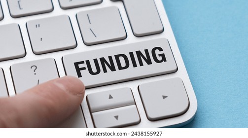 Close-up image of a white computer keyboard with a finger pressing the white button with black text Funding. The keyboard is on a blue background, highlighting the concept of financial transactions.