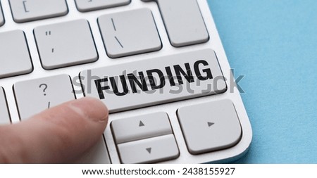 Close-up image of a white computer keyboard with a finger pressing the white button with black text Funding. The keyboard is on a blue background, highlighting the concept of financial transactions.