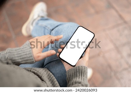 A close-up image of a white-screen smartphone mockup in a woman's hand with a blurred background. A woman using her smartphone outdoors. people and wireless technology concepts