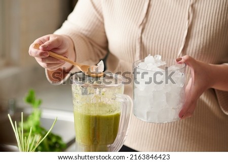 Close-up image of woman adding ice cubes in green smoothie