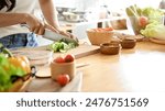 A close-up image of a woman cutting lettuces on a cutting board at a wooden kitchen tabletop, cooking in the kitchen. healthy food, lifestyle, home cooking