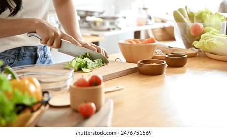 A close-up image of a woman cutting lettuces on a cutting board at a wooden kitchen tabletop, cooking in the kitchen. healthy food, lifestyle, home cooking - Powered by Shutterstock