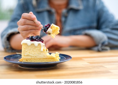Closeup image of a woman eating blueberry cheesecake with spoon
