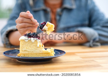 Closeup image of a woman eating blueberry cheesecake with spoon