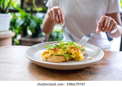 Closeup image of a woman eating scrambled eggs and avocado open sandwich - Powered by Shutterstock