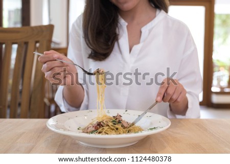 Closeup image of a woman eating spicy bacon spaghetti on wooden table