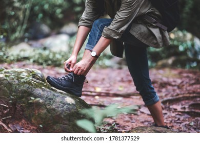 Closeup image of a woman hiker tying shoelaces and getting ready for trekking in the forest