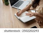 A close-up image of a woman holding a pen, writing something in a book, working at a desk indoors. doing homework, writing diary, making list, lecturing