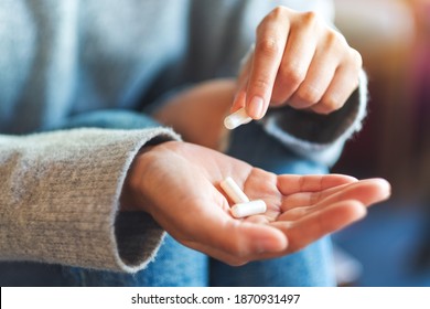 Closeup image of a woman holding and picking white medicine capsules in hand