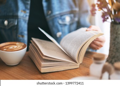 Closeup image of a woman holding and reading a vintage novel book while drinking coffee