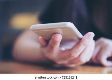 Closeup image of a woman holding and using smart phone in modern cafe