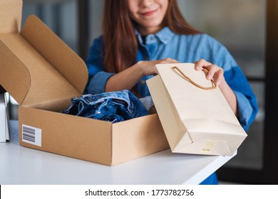 Closeup Image Of A Woman Opening And Looking Inside Shopping Bag With Postal Parcel Box Of Clothing For Delivery And Online Shopping Concept