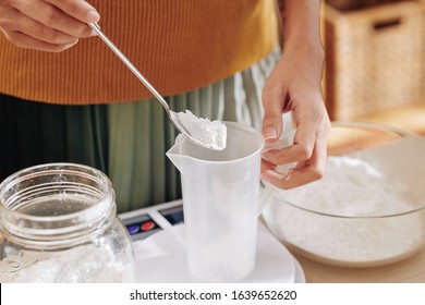 Close-up Image Of Woman Putting Spoon Of Lye In Plastic Jar When Making Soap At Home