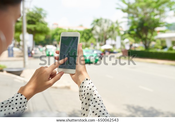 Close-up image of woman tracking taxi car on\
her smartphone