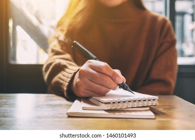 Closeup Image Of A Woman Writing On Blank Notebook With Fountain Pen On Wooden Table