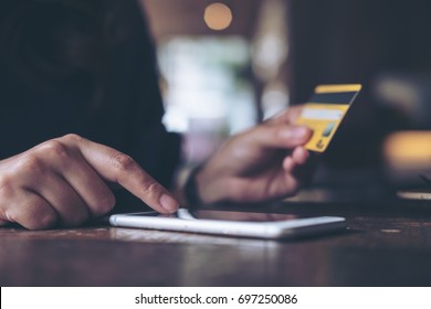 Closeup image of a woman's hand holding credit card and pressing at mobile phone on wooden table in office