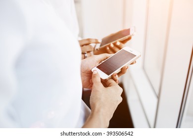Closeup image of a women are chatting in network on their cell telephones during free time in work day. Two female are reading text message on mobile phones, while are standing in office interior