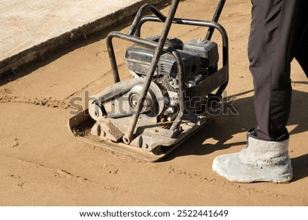 A close-up image of worker operating a vibrating soil compactor used to compact soil in preparation for paving stones. High quality photo