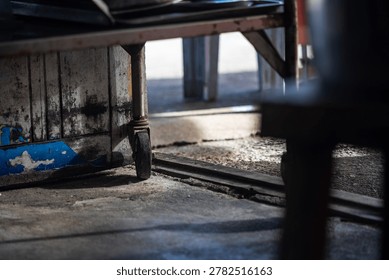 Close-up image of a workshop or storage area showing support beams, a concrete floor, and a wooden platform. Focus on structural details and texture.