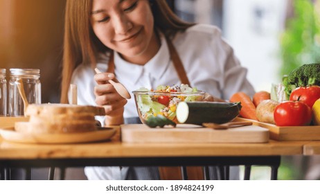 Closeup Image Of A Young Asian Female Chef Cooking And Eating Fresh Mixed Vegetables Salad In Kitchen