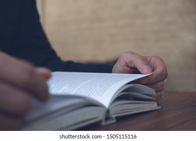 Closeup Image Of Young Asian Man Reading A Book. Casual Man, Student Opening And Relaxed Reading Book On Wooden Table In University Library, Vintage Style.