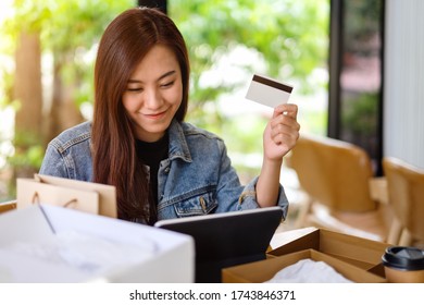 Closeup Image Of A Young Asian Woman Using Tablet Pc And Credit Card For Online Shopping With Postal Parcel Box And Shopping Bags On The Table