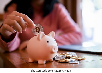 close-up image, Young Asian woman insert golden bitcoin into a pink piggy bank. investment and money saving concept