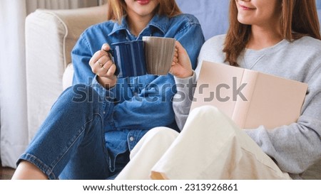 Closeup image of a young couple women holding book, clinking and drinking coffee together