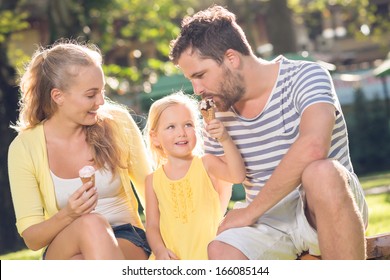 Close-up image of a young happy family spending their weekend in the park where the daughter feeding her father with the ice-cream  - Powered by Shutterstock