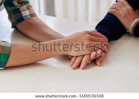Close-up image of young man holding hand of his mother when reassuring her