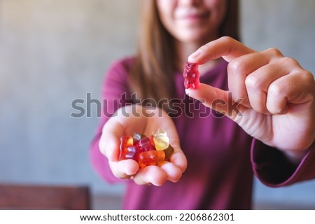 Closeup image of a young woman holding and showing at a red jelly gummy bears