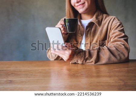 Closeup image of a young woman holding and using mobile phone while drinking coffee in cafe
