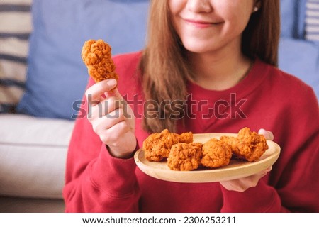 Closeup image of a young woman holding and eating fried chicken at home