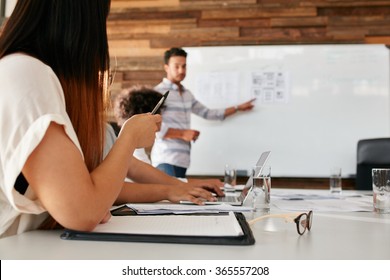 Closeup image of young woman sitting in a meeting in boardroom with man giving presentation in background. Focus on hands of female executive. - Shutterstock ID 365557208