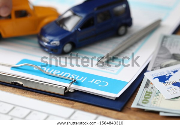 Close-up of important\
papers about car assurance. Credit bank card and currency money\
lying on table. Blue and orange toy cars on folder. Advertisement\
and business concept