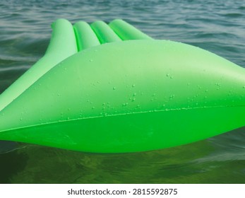 A closeup of a inflatable pool float lounge mattress drifting on water, classic ribbed vinyl water rafts, with integrated raised pillow headrest, for sunbathing, lounging, and drifting on pool, lake, or beach waters
