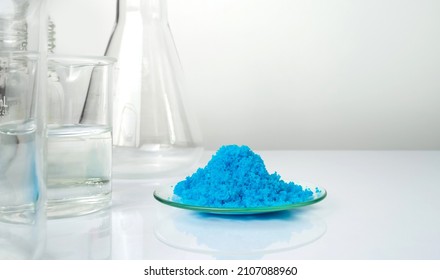 Closeup inorganic chemical on white laboratory table. Copper(II) sulfate in Chemical Watch Glass place next to alcohol liquid in Beaker. Chemical ingredient for Cosmetics and Toiletries product.
