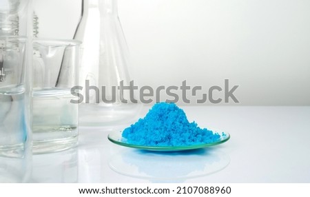 Closeup inorganic chemical on white laboratory table. Copper(II) sulfate in Chemical Watch Glass place next to alcohol liquid in Beaker. Chemical ingredient for Cosmetics and Toiletries product.