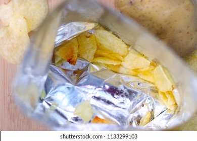 Closeup inside empty foil bag of potato chips. Fresh raw potatoes lying. Opened snack bag.