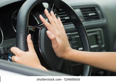 Closeup inside vehicle of hand pushing on steering wheel honking horn, black interior background, female driver concept