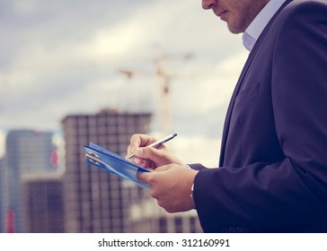 Close-up Inspector  Holding Clipboard On The Background Of Construction  