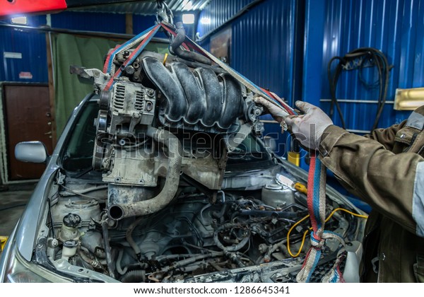 Close-up of the installation of the\
motor on an old car using a pneumatic manual crane in the auto\
repair shop. The work of auto mechanics to remove the\
engine