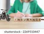 Close-up of insurance word on wooden blocks in row and small model of motorbike. Insurance broker on background.