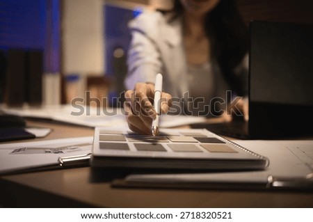 Close-up of an interior designer pointing at surface material swatches while choosing textures catalog for a design project at night.