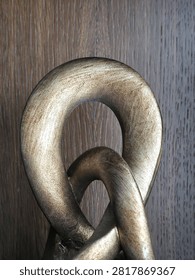 Close-up of interlocking metallic bronze and gold sculptural rings showing brushed antique textures, curved abstract shapes, and dark wood background.