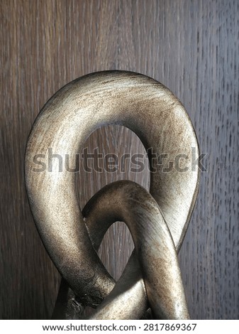 Close-up of interlocking metallic bronze and gold sculptural rings showing brushed antique textures, curved abstract shapes, and dark wood background.